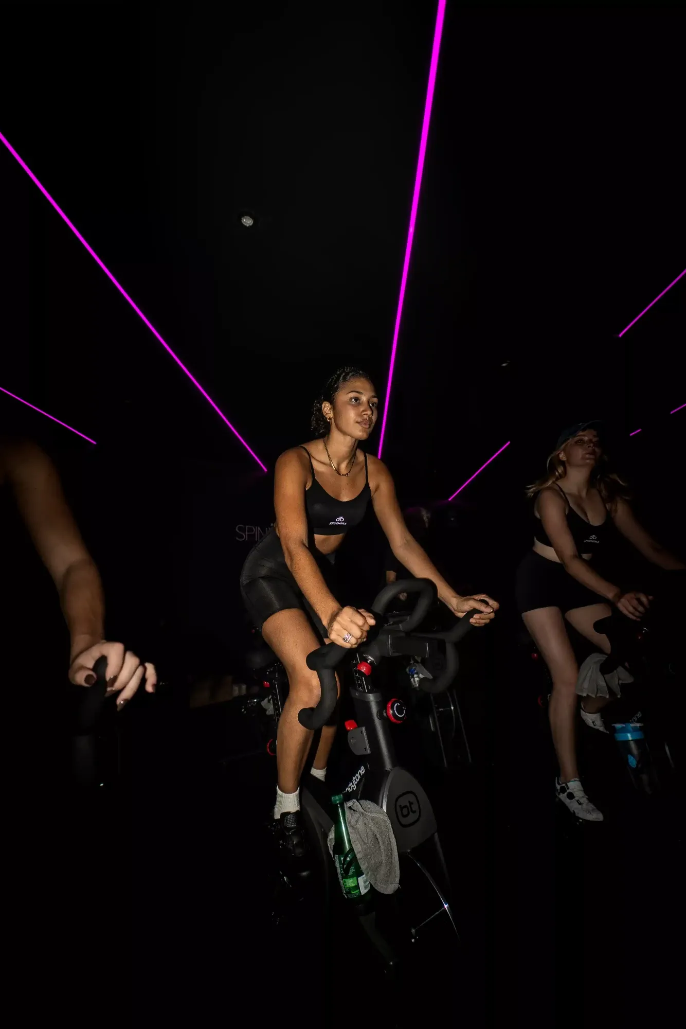 Une participante pédale sous les faisceaux laser magenta du studio Spinners Cycling à Toulouse, une autre cycliste à ses côtés