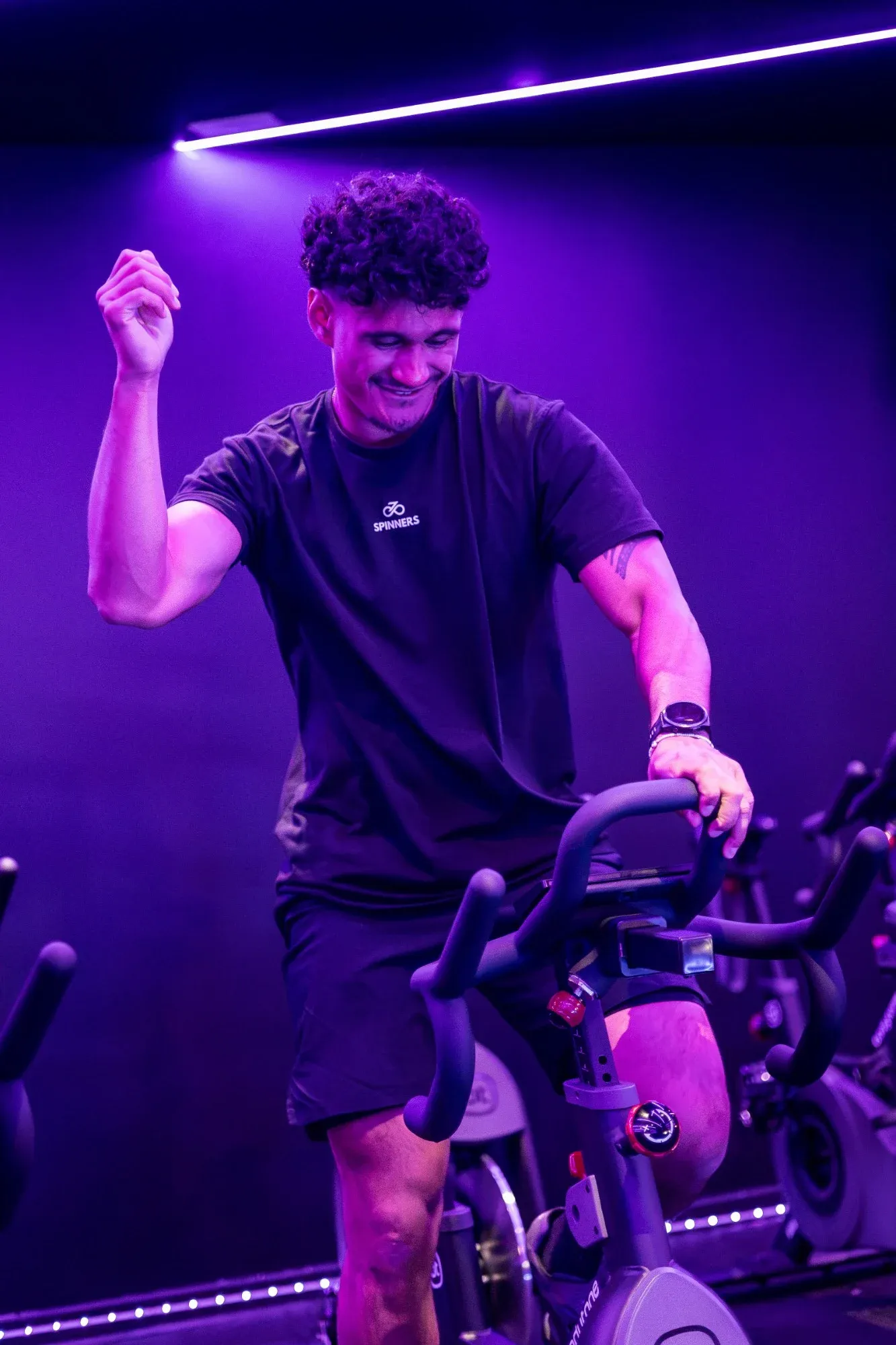 Un coach de Spinners Cycling lance le rythme depuis son vélo, sous les néons violets du studio toulousain