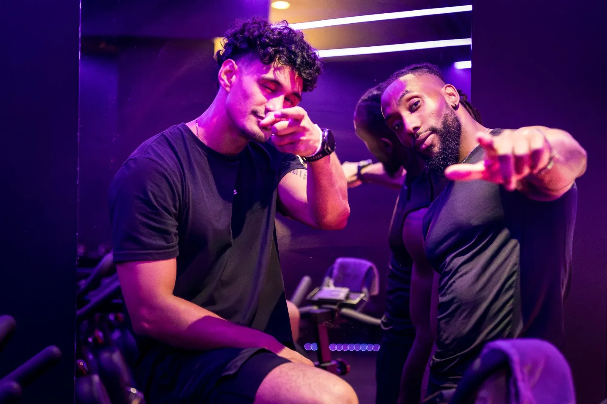 Les deux coachs de Spinners Cycling, assis sur leurs vélos, sous les lumières violettes du studio toulousain