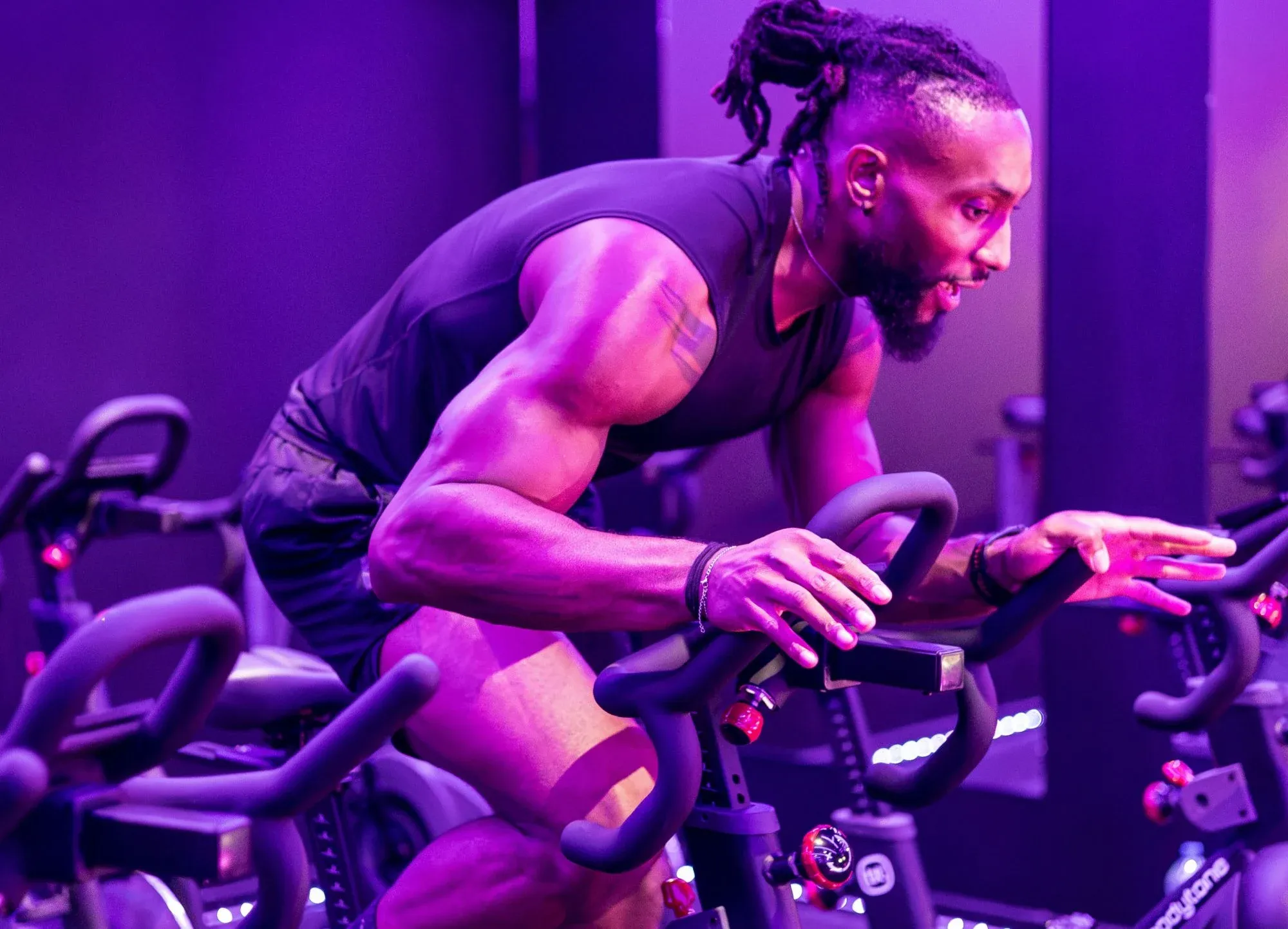Un coach de Spinners Cycling penché sur son vélo pendant un cours, sous les lumières violettes du studio toulousain